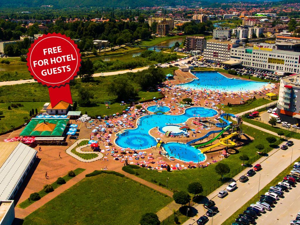 Hotel Hills Sarajevo Congress & Thermal Spa Resort Ilidža Ngoại thất bức ảnh The photo shows an aerial view of a large swimming pool area, likely part of a hotel or resort. There are several pools of different shapes and sizes, including one that resembles a Mickey Mouse shape. The area is filled with numerous sun loungers an